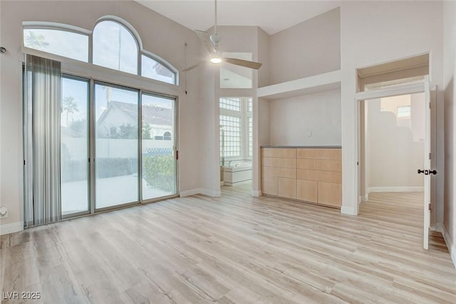 unfurnished living room featuring a ceiling fan, light wood-style flooring, baseboards, and a high ceiling