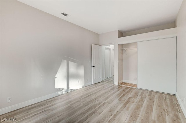 unfurnished bedroom with wood finished floors, visible vents, a closet, and baseboards