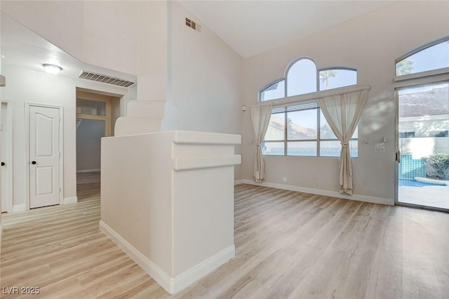 interior space featuring visible vents, baseboards, an upstairs landing, light wood-style floors, and high vaulted ceiling