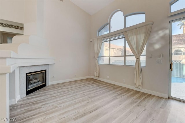 unfurnished living room with a tiled fireplace, high vaulted ceiling, baseboards, and wood finished floors