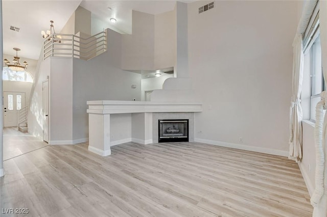 unfurnished living room with visible vents, an inviting chandelier, light wood-style flooring, and a towering ceiling