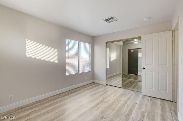 unfurnished bedroom with baseboards, visible vents, a closet, and light wood-type flooring