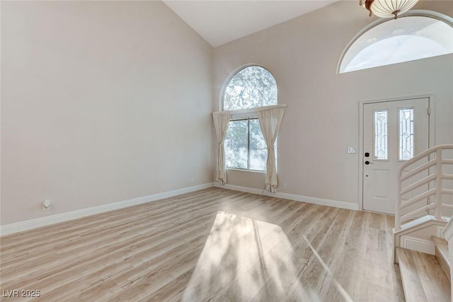 entryway featuring baseboards, high vaulted ceiling, and light wood-style flooring