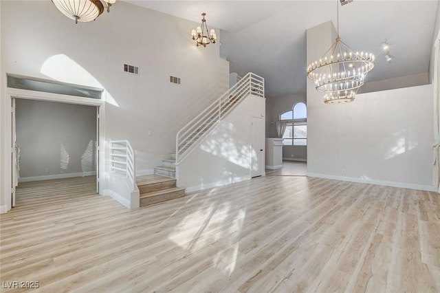 unfurnished living room featuring a notable chandelier, stairs, visible vents, and wood finished floors