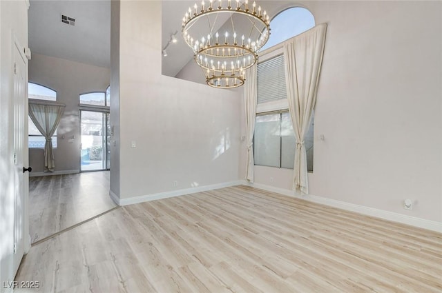 empty room with an inviting chandelier, wood finished floors, visible vents, and baseboards