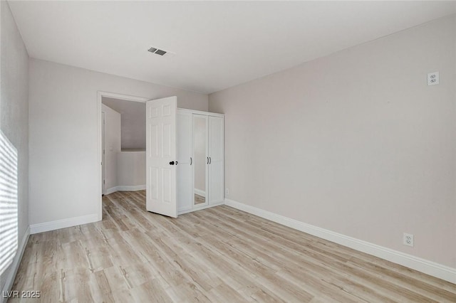 unfurnished bedroom with light wood-style flooring, baseboards, visible vents, and a closet