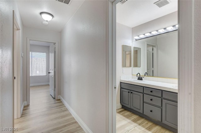 bathroom with visible vents, a sink, wood finished floors, double vanity, and baseboards