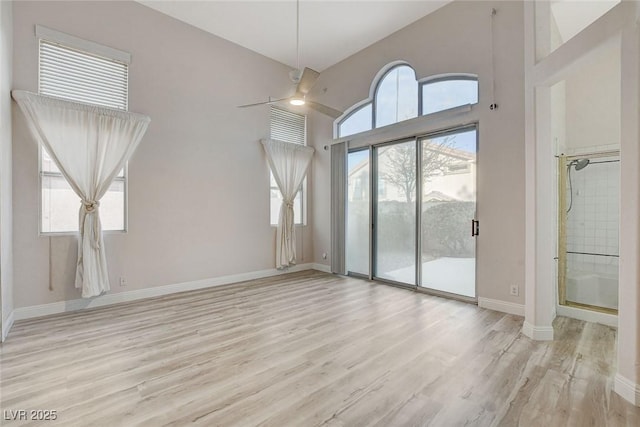 unfurnished living room with ceiling fan, baseboards, wood finished floors, and a towering ceiling