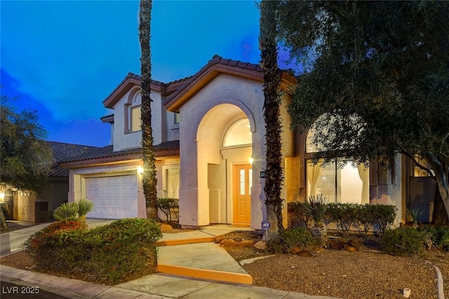 mediterranean / spanish-style home featuring stucco siding, a tiled roof, and a garage