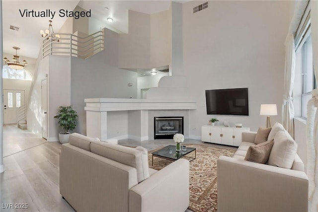 living area featuring visible vents, a notable chandelier, wood finished floors, a high ceiling, and a fireplace