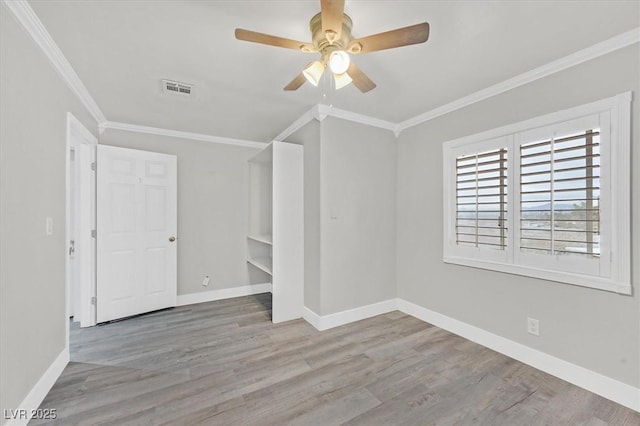 spare room with baseboards, visible vents, wood finished floors, and ornamental molding