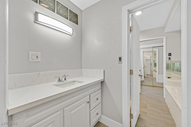 bathroom with a textured wall, wood finished floors, vanity, baseboards, and a bath