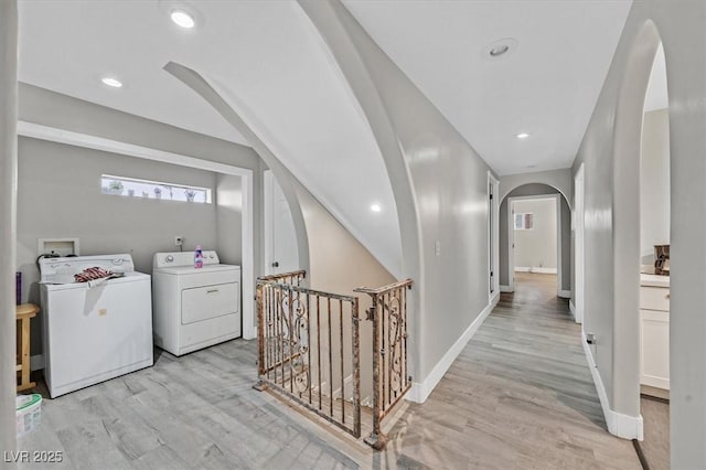 hall with arched walkways, light wood finished floors, an upstairs landing, and washer and dryer