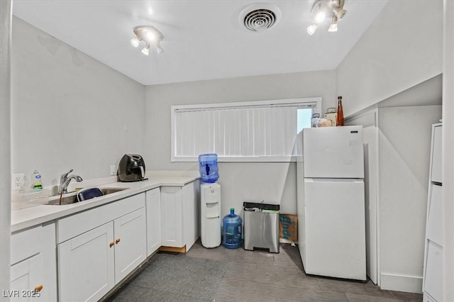 kitchen featuring visible vents, freestanding refrigerator, light countertops, white cabinetry, and a sink