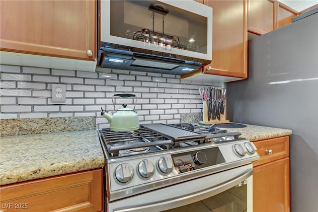 kitchen featuring stainless steel appliances, brown cabinets, light stone counters, and decorative backsplash