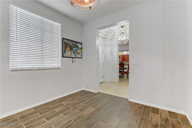 spare room featuring wood tiled floor, a chandelier, and baseboards