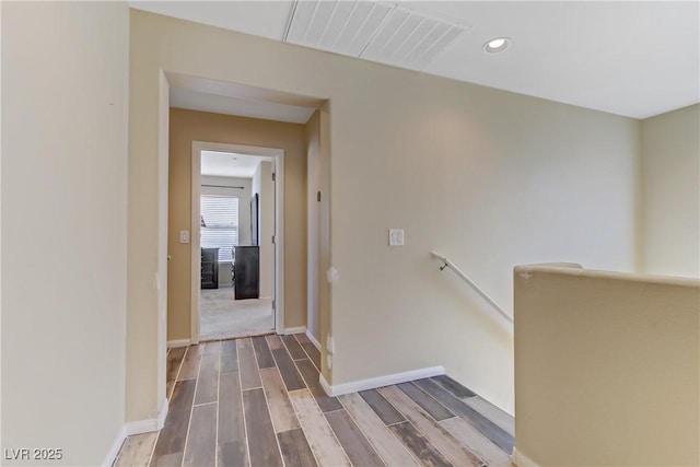 corridor with wood tiled floor, visible vents, baseboards, and an upstairs landing