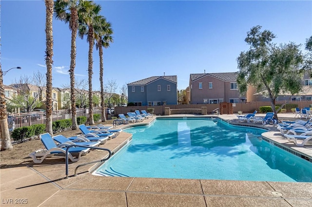 community pool with a patio area, fence, and a residential view