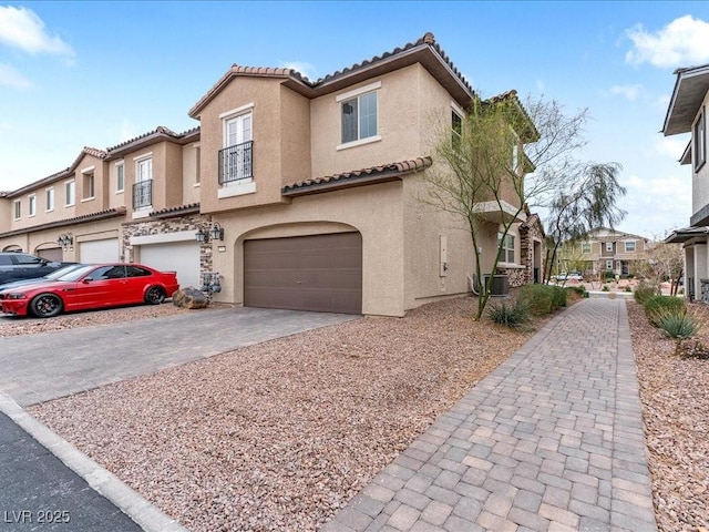 mediterranean / spanish-style house with central AC unit, a tiled roof, an attached garage, decorative driveway, and stucco siding