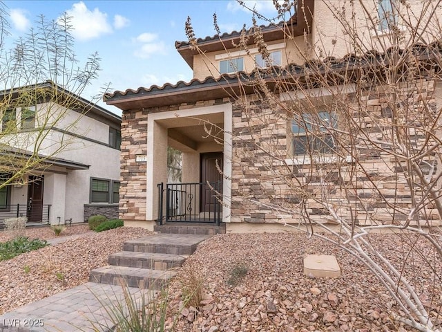 doorway to property featuring stone siding, a tiled roof, and stucco siding