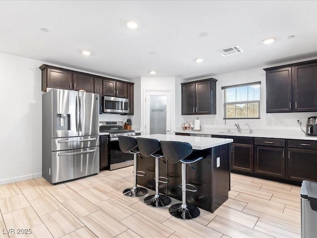 kitchen with a center island, stainless steel appliances, light countertops, visible vents, and a sink