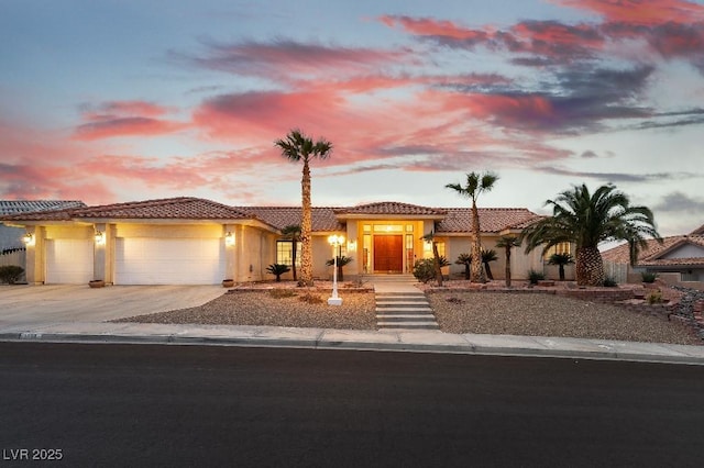 mediterranean / spanish-style house featuring a garage, a tile roof, concrete driveway, and stucco siding