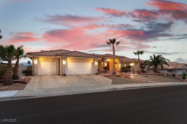 mediterranean / spanish house featuring driveway, a tiled roof, an attached garage, and stucco siding