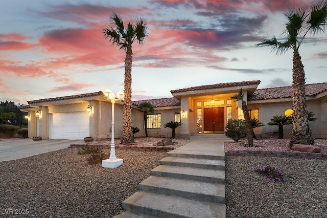 mediterranean / spanish home featuring a garage, concrete driveway, a tiled roof, and stucco siding