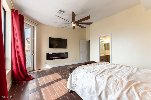 bedroom featuring visible vents, a glass covered fireplace, wood tiled floor, ensuite bath, and baseboards