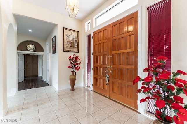 foyer entrance with light tile patterned floors, baseboards, and arched walkways