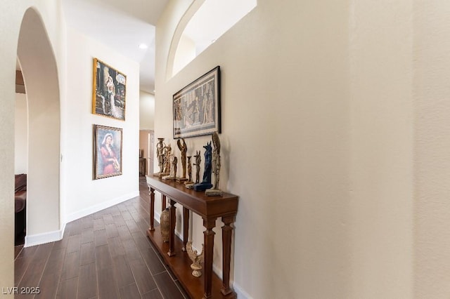 hall with dark wood-type flooring, arched walkways, and baseboards