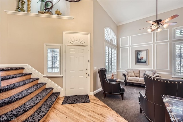 foyer entrance with ceiling fan, high vaulted ceiling, wood finished floors, ornamental molding, and stairway