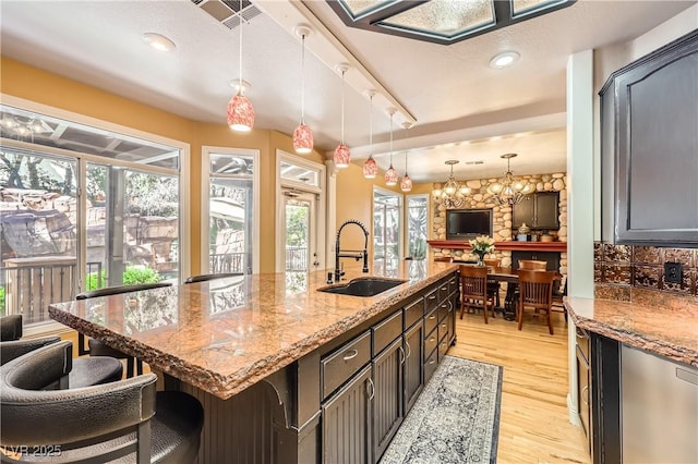 kitchen with visible vents, a breakfast bar area, light stone counters, light wood-style floors, and a sink