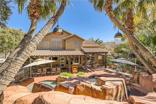 rear view of property featuring an outdoor fire pit, a tiled roof, an in ground hot tub, a patio area, and stucco siding