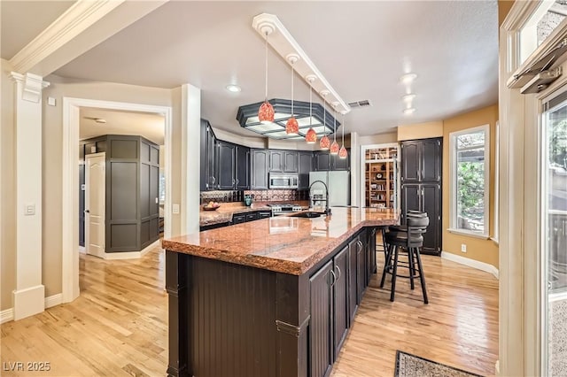 kitchen featuring light wood-style floors, visible vents, stainless steel microwave, and a breakfast bar