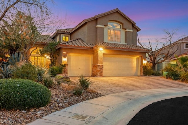 mediterranean / spanish house featuring decorative driveway, a tile roof, stucco siding, a garage, and stone siding