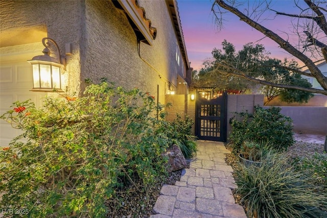 property exterior at dusk featuring a gate and stucco siding