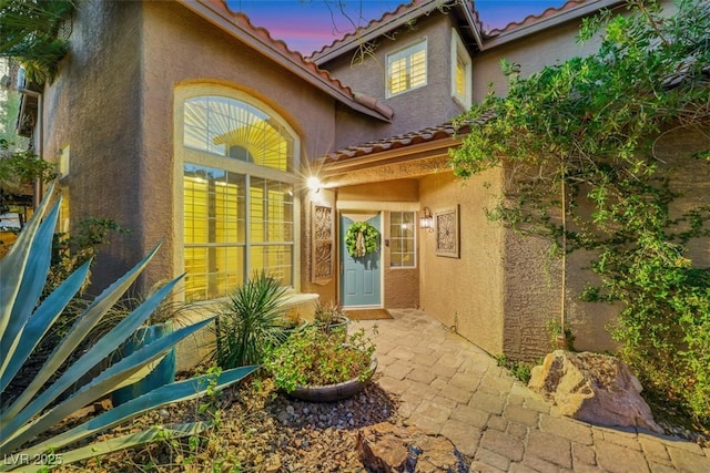 exterior entry at dusk featuring a tile roof and stucco siding