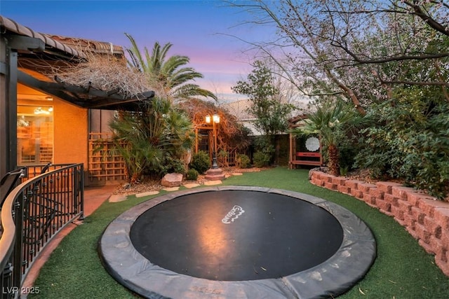 pool at dusk with a trampoline and fence