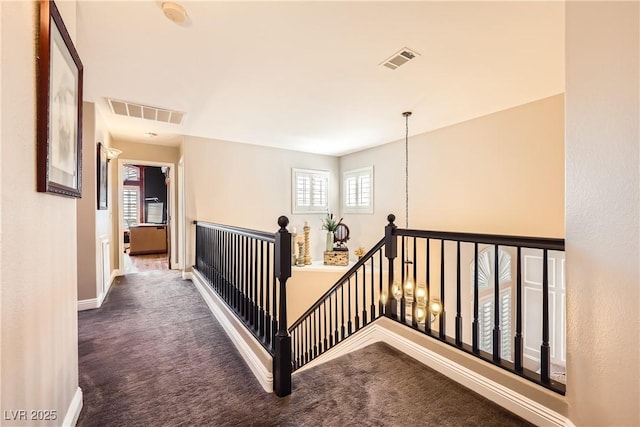 hallway featuring carpet flooring, visible vents, and an upstairs landing