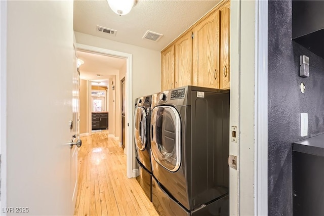 laundry room with light wood-type flooring, visible vents, cabinet space, and washing machine and clothes dryer