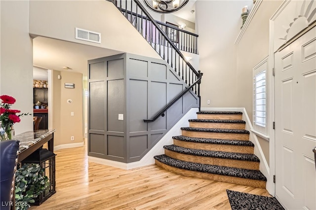 stairs with visible vents, a towering ceiling, baseboards, and wood finished floors