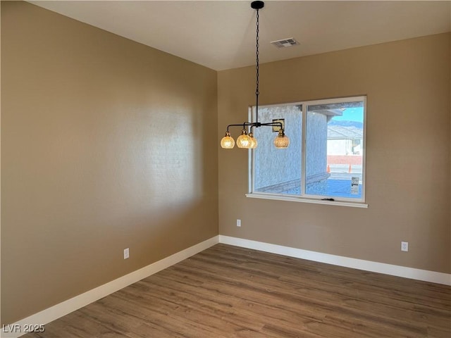 spare room featuring a chandelier, visible vents, baseboards, and wood finished floors