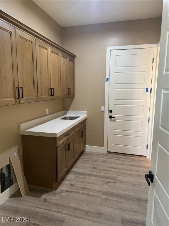 laundry room with light wood-style floors, baseboards, and a sink