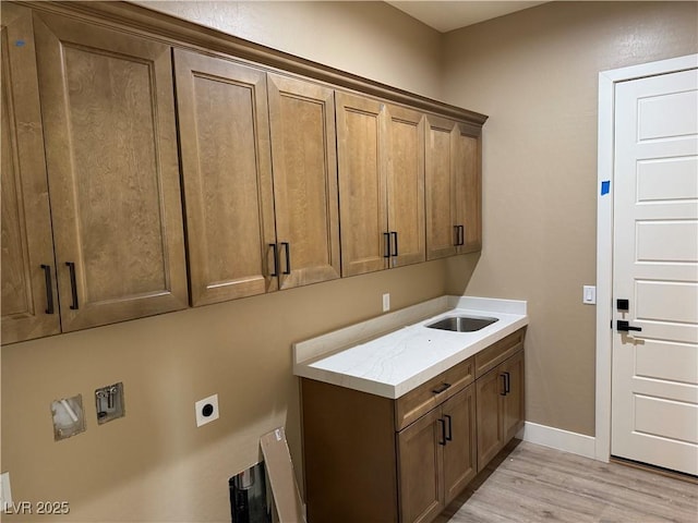 washroom featuring a sink, baseboards, cabinet space, light wood finished floors, and electric dryer hookup