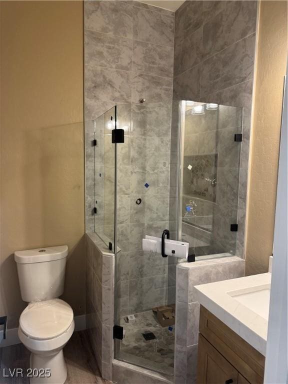 full bathroom with toilet, a shower stall, baseboards, and vanity