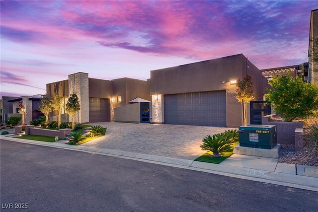 adobe home featuring decorative driveway, an attached garage, and stucco siding