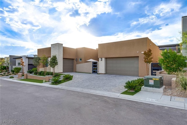 pueblo-style house featuring decorative driveway, an attached garage, and stucco siding