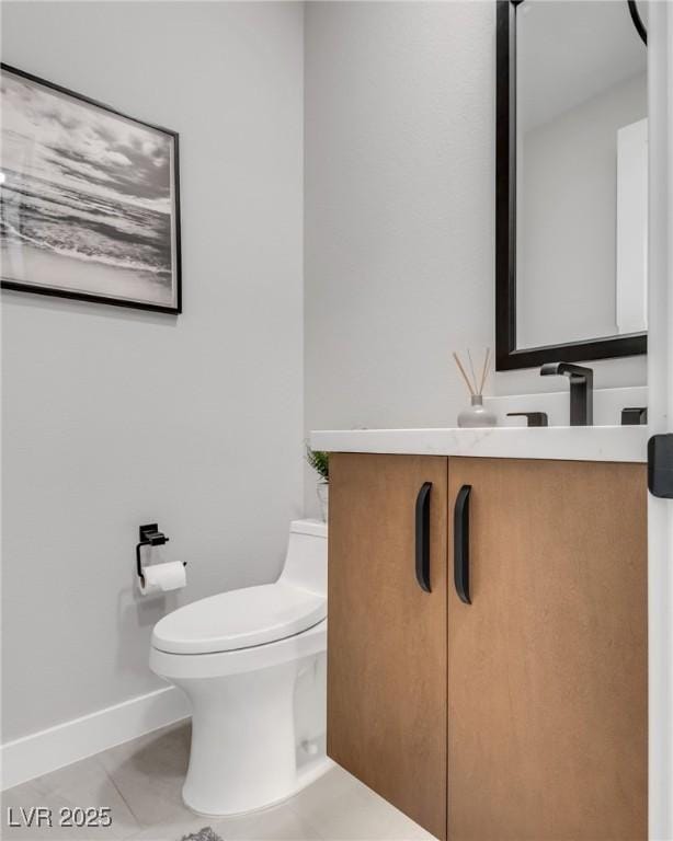 half bathroom featuring toilet, tile patterned floors, baseboards, and vanity