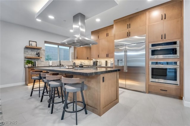 kitchen featuring island range hood, stainless steel appliances, a breakfast bar, backsplash, and a center island